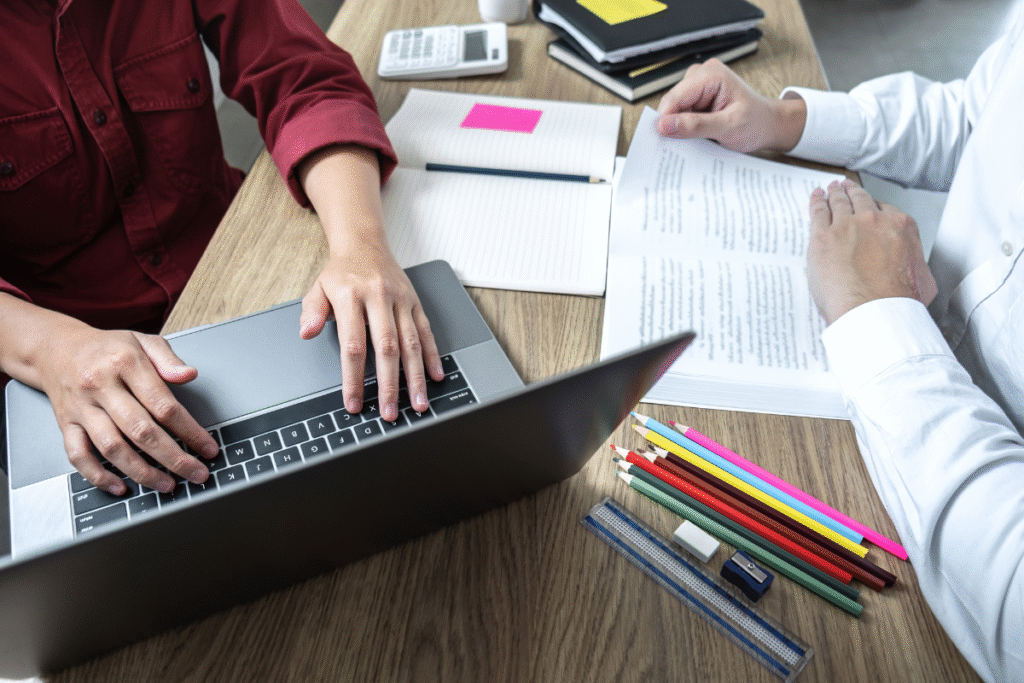 Students preparing for exams and assignments with a laptop, textbooks, and study notes during a tutoring session.